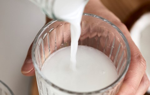 Kokosmilch wird aus einer Glasflasche in ein Glas geschüttet